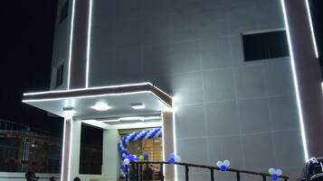 Un hotel con una facciata moderna, insegne illuminate e un ingresso accogliente con gradini e un arco decorativo.