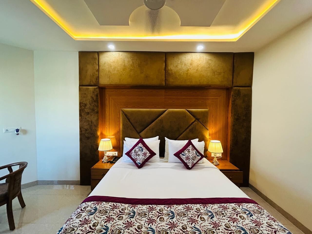 A hotel room with a large bed, two bedside tables with lamps, a wooden headboard, and a ceiling light fixture.