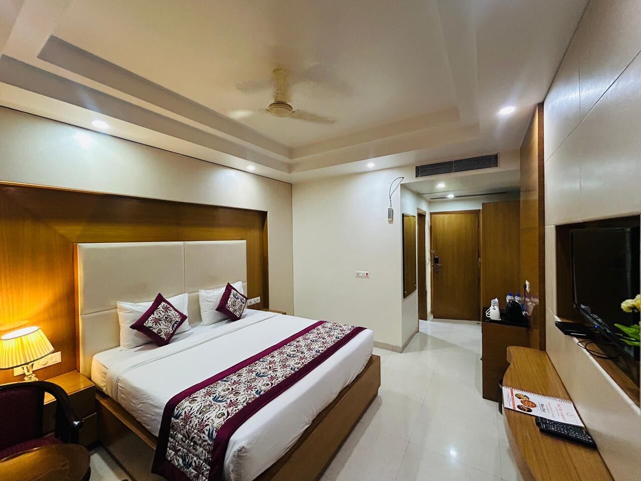 A hotel room with a large bed, a desk, a TV, and a wardrobe.