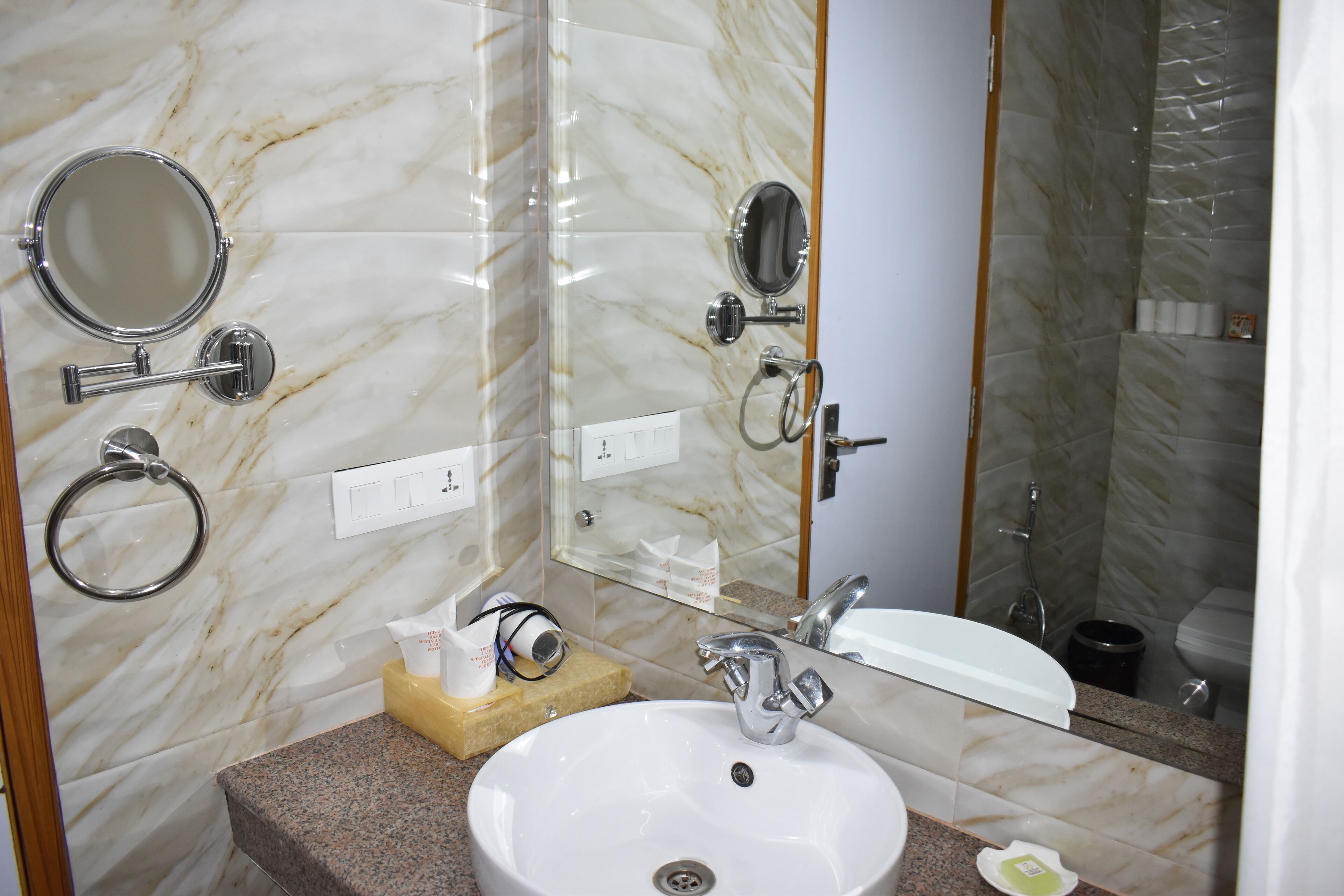 Un baño con pared de mármol, un lavamanos, un espejo y una ducha.