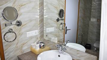 Un baño con pared de mármol, un lavamanos, un espejo y una ducha.