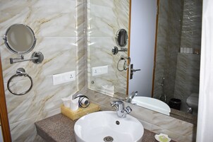 Un baño con pared de mármol, un lavamanos, un espejo y una ducha.