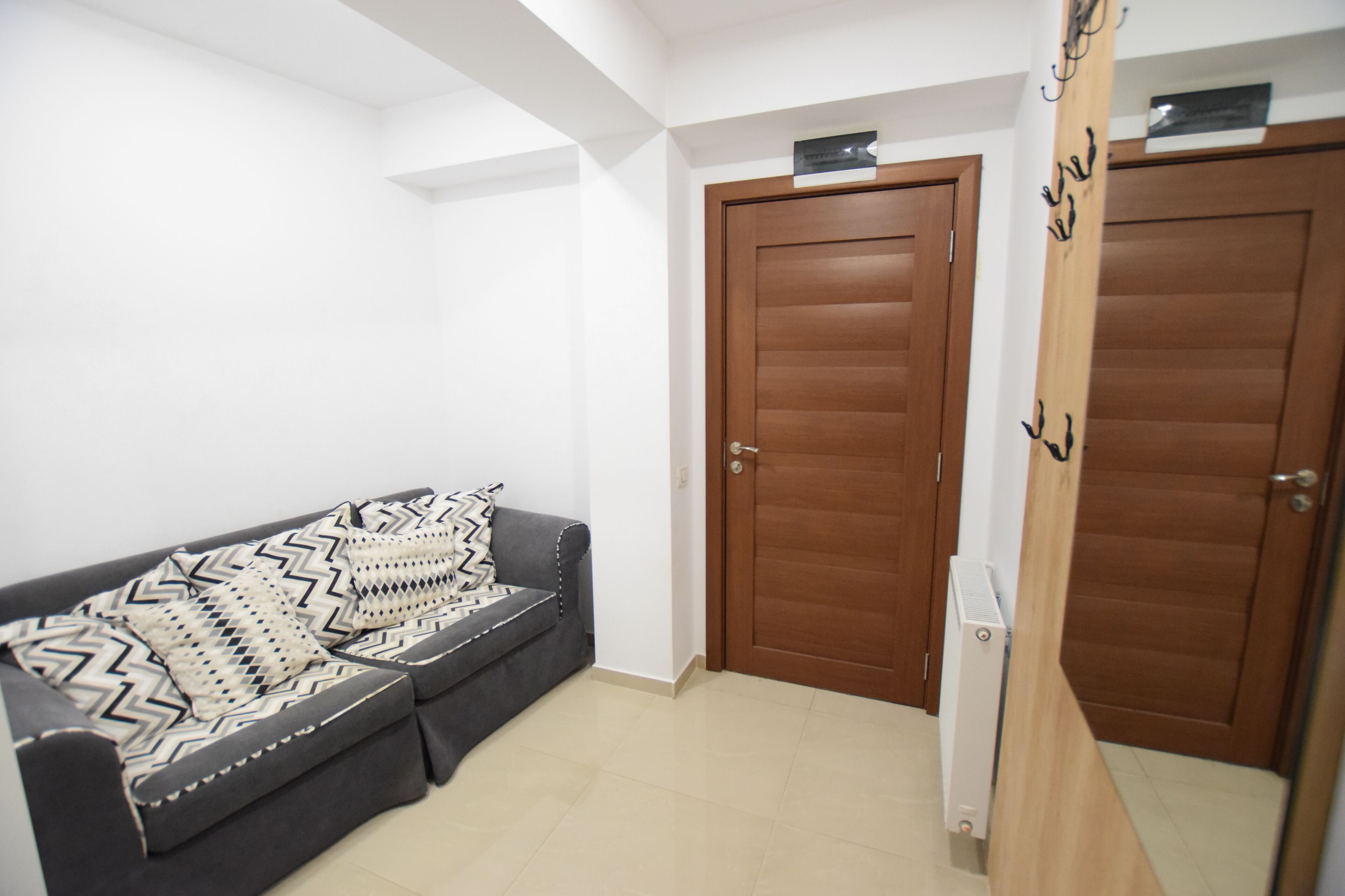 A room with a grey sofa, two wooden doors, and a white wall.