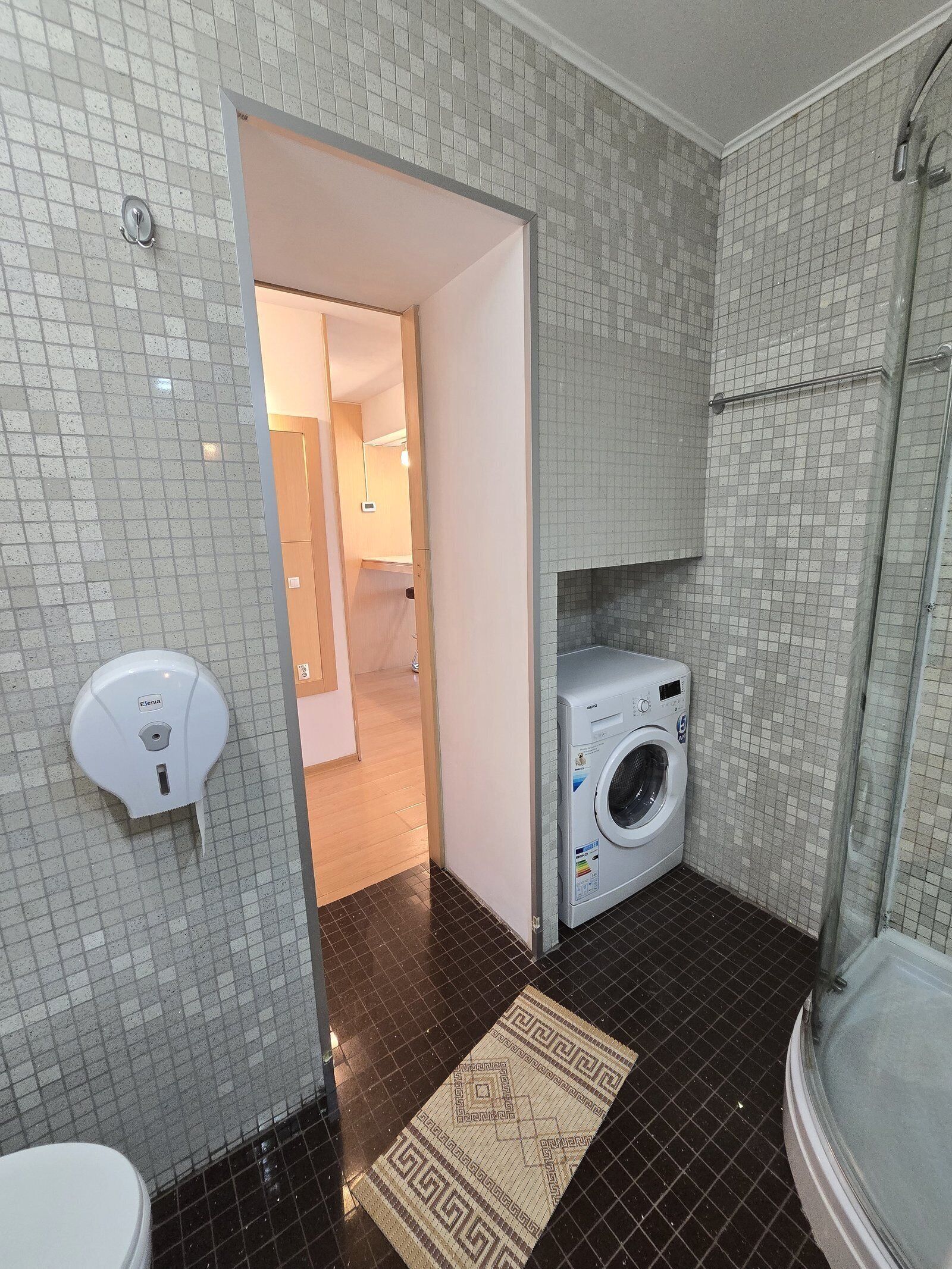 A bathroom with a tiled floor, a washing machine, a toilet, and a hand dryer.