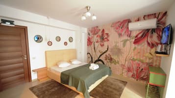 A bedroom with a bed, a green bedspread, a wall-mounted air conditioner, a television, and a floral wallpaper.
