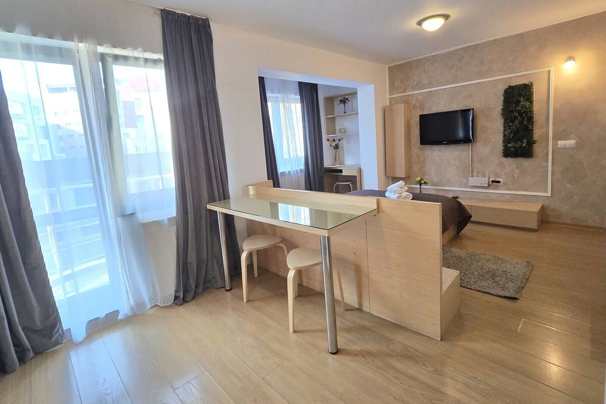 A modern living room with a glass-top dining table, a sofa, and a TV mounted on the wall.