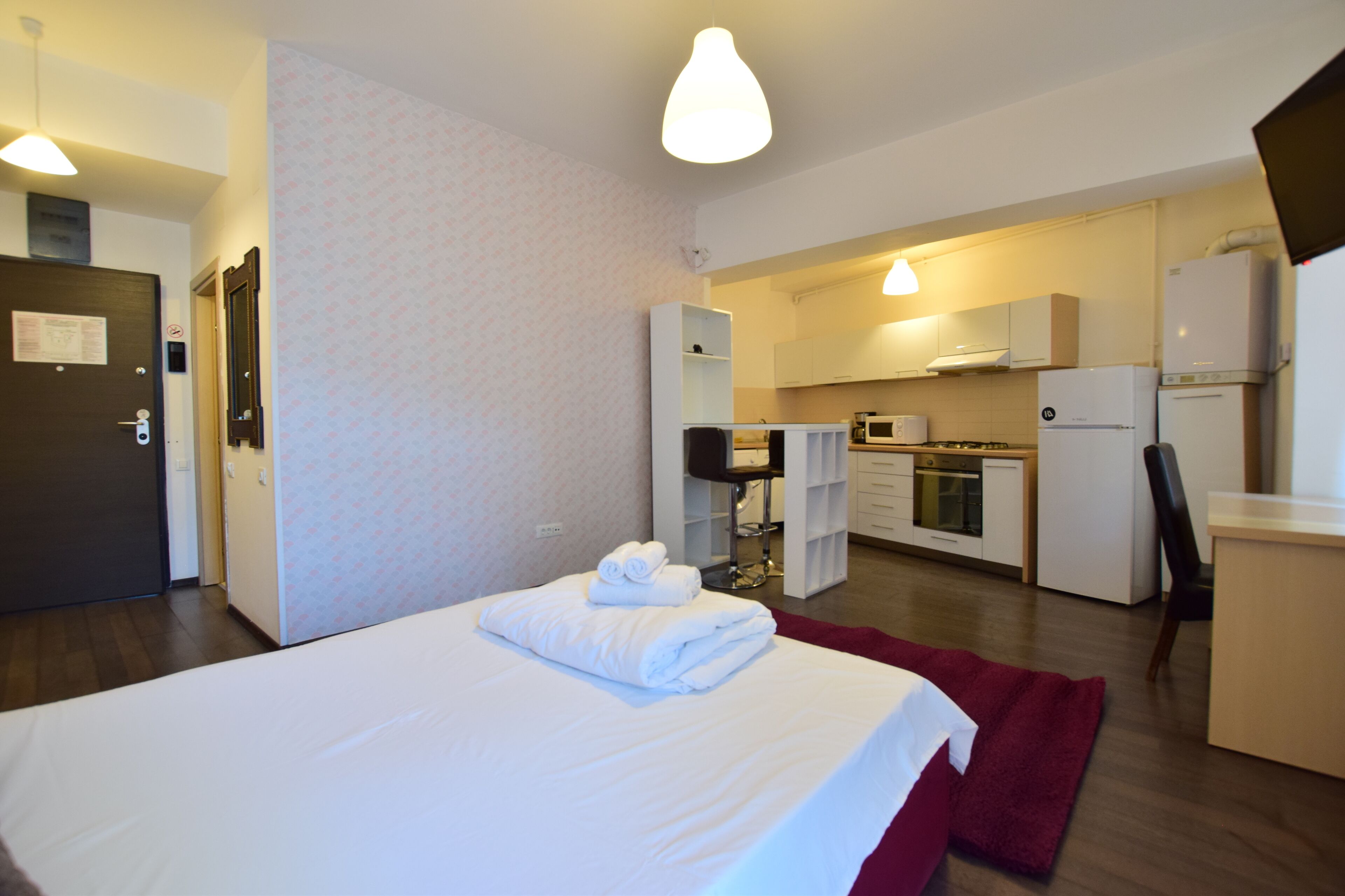 A hotel room with a bed, a desk, a chair, a microwave, a refrigerator, and a small kitchenette.