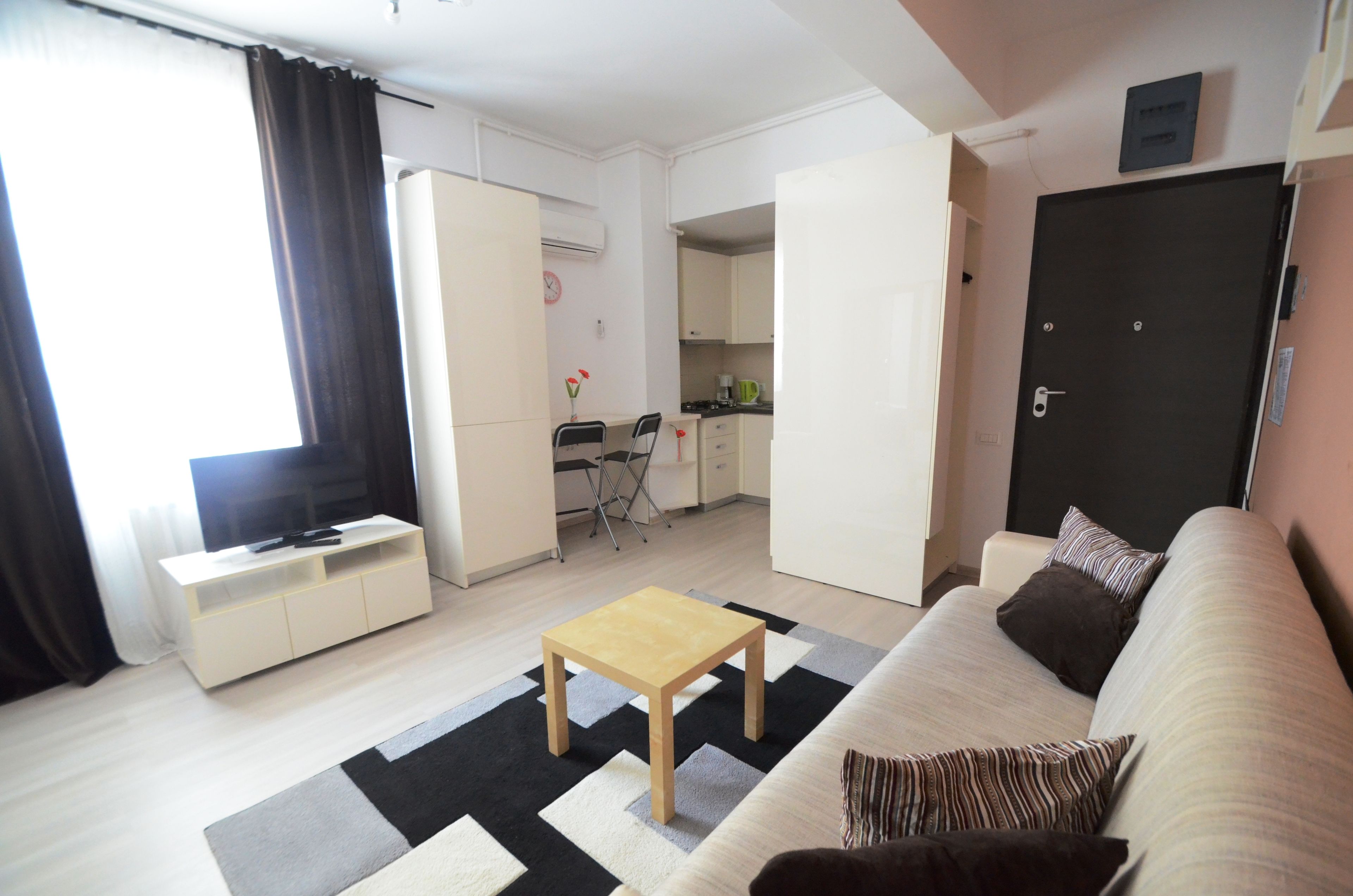 Un espace de vie compact comprenant un canapé, une table basse, un téléviseur, un coin cuisine et une porte.