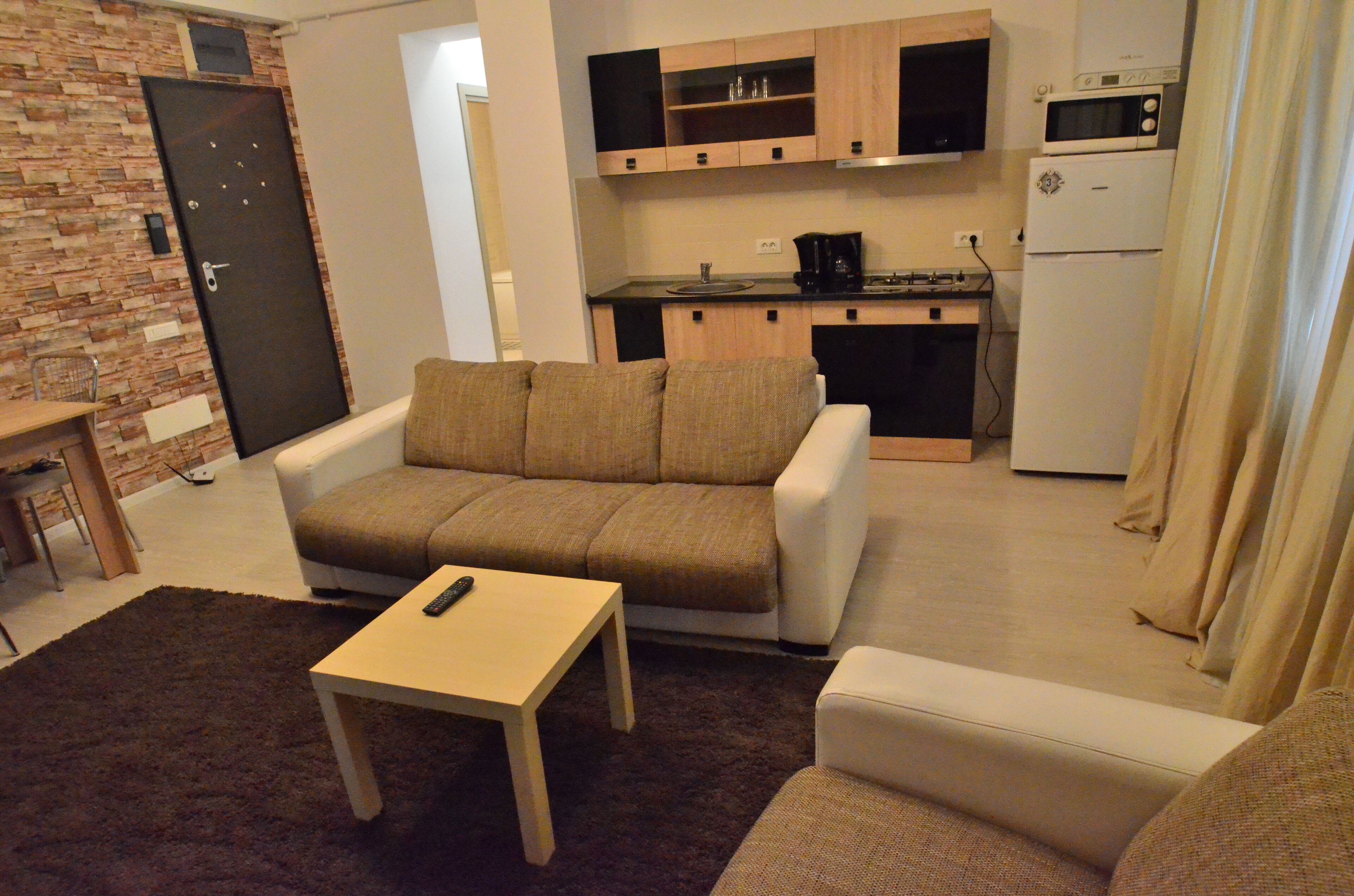 Un espacio habitable compacto con sofá, una mesita, una kitchenette con microondas y refrigerador, y una puerta con cerradura.