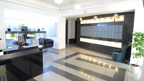 A modern reception area with a black reception desk, a digital display, and a seating area with a blue chair. - Uptown Residence Apartments (Bucharest)
