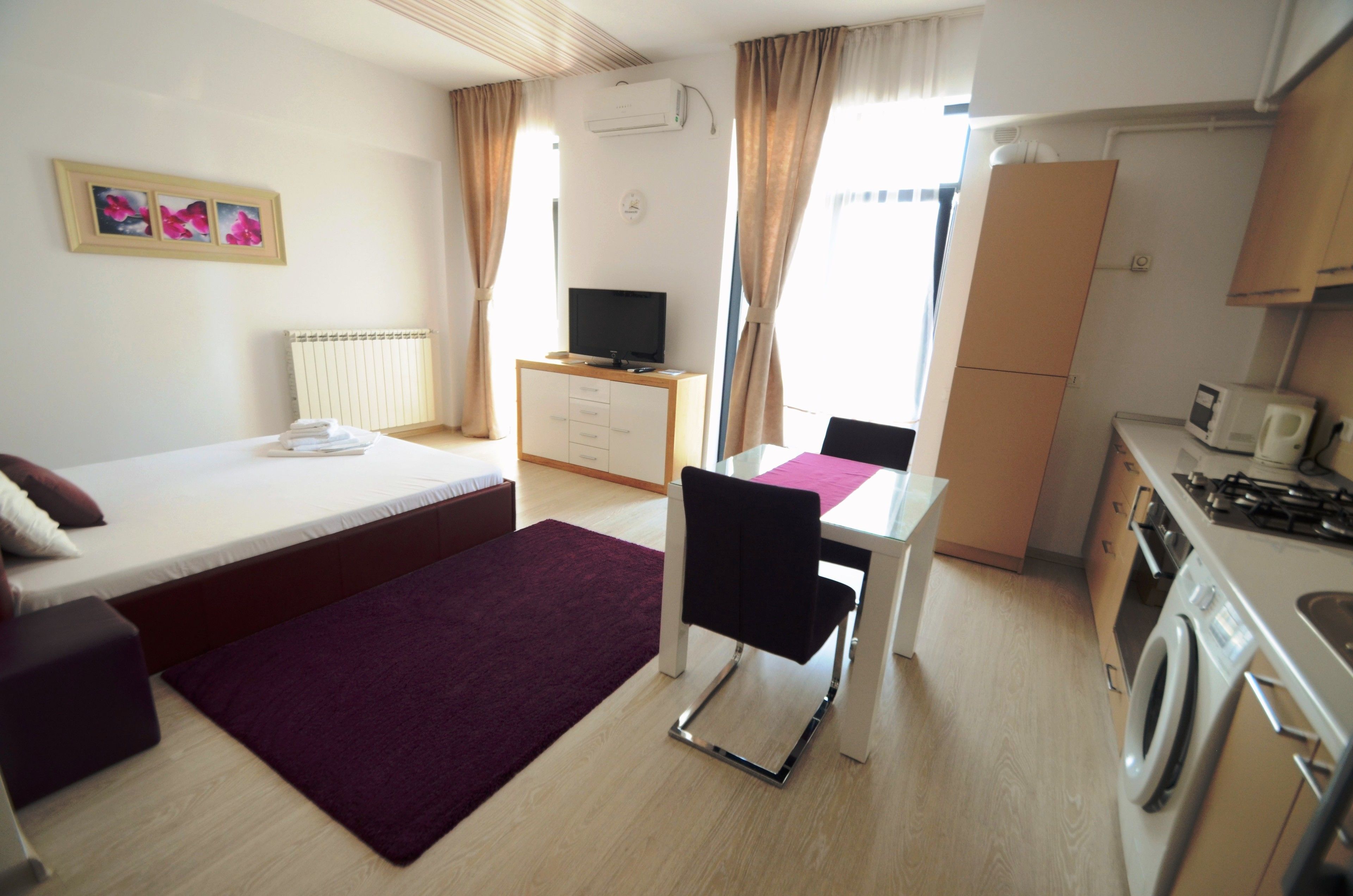 Une chambre d’hôtel compacte comprenant un lit, un bureau, une chaise, une télévision, un lave-linge et une kitchenette.