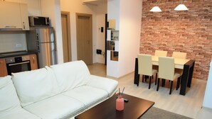 A modern living room with a white sofa, a dark coffee table, and a dining area with a brick wall and pendant lights. - Uptown Residence Apartments (Bucharest)