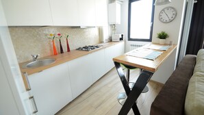 A modern kitchen with white cabinets, a wooden countertop, and a black chair. - Uptown Residence Apartments (Bucharest)