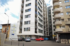 Un edificio residencial de varios pisos con balcones, un cartel que dice Uptown Residence, y coches estacionados en la calle.