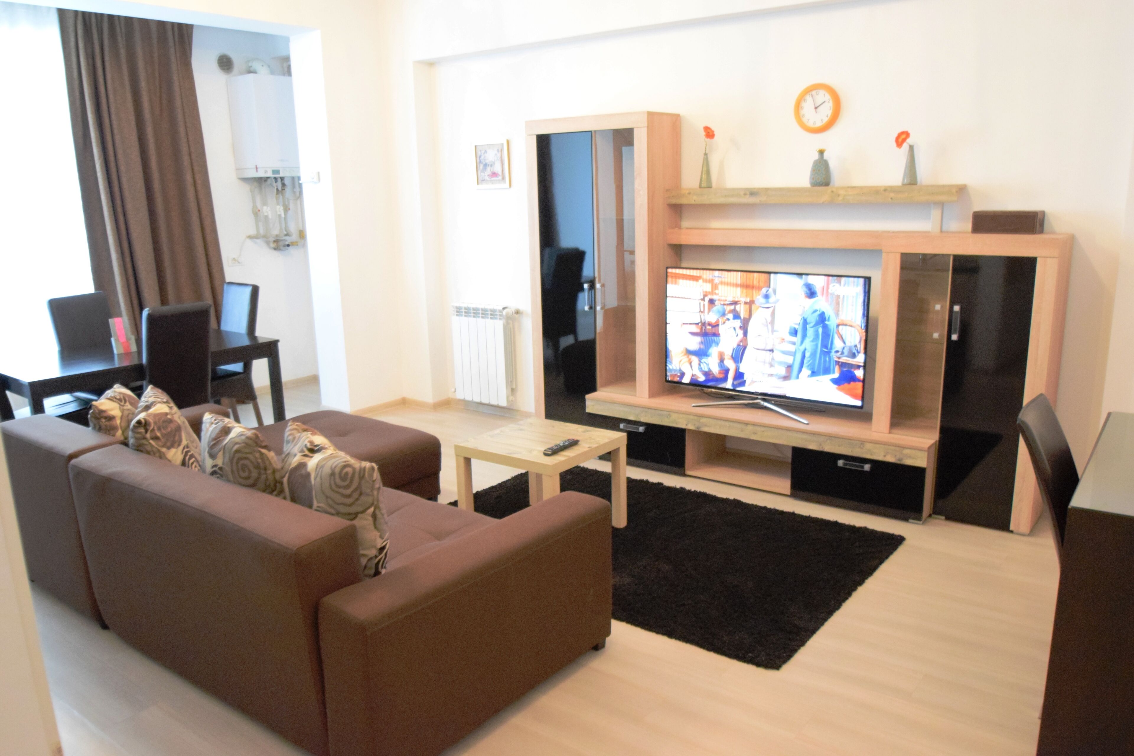 A living room with a brown sofa, a coffee table, a TV on a wooden stand, and a black rug.