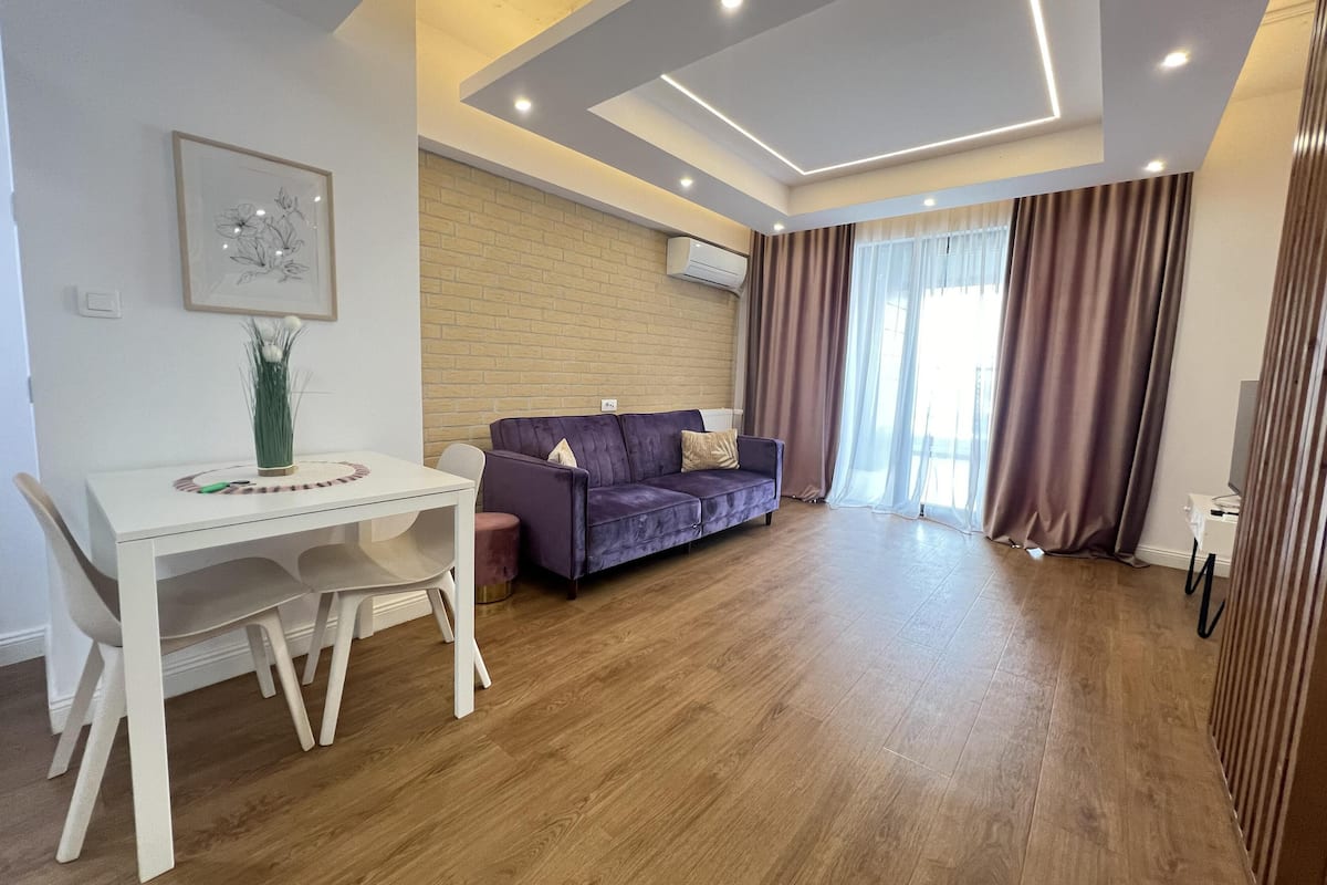 Una sala de estar moderna con una mesa blanca, un sofá morado y suelo de madera.