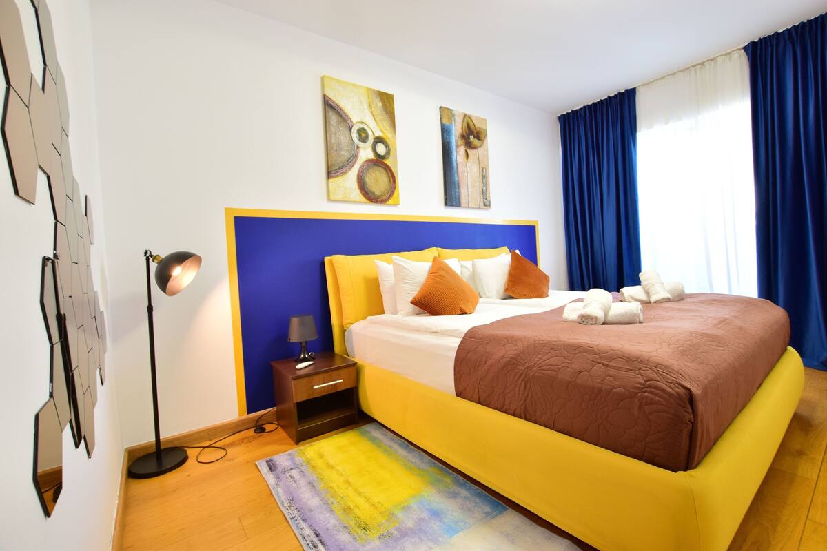 Un dormitorio moderno con una cama grande, una mesita de noche, una lámpara y arte abstracto en la pared.