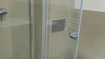 Ducha con cerramiento de vidrio, inodoro blanco y un estante pequeño.