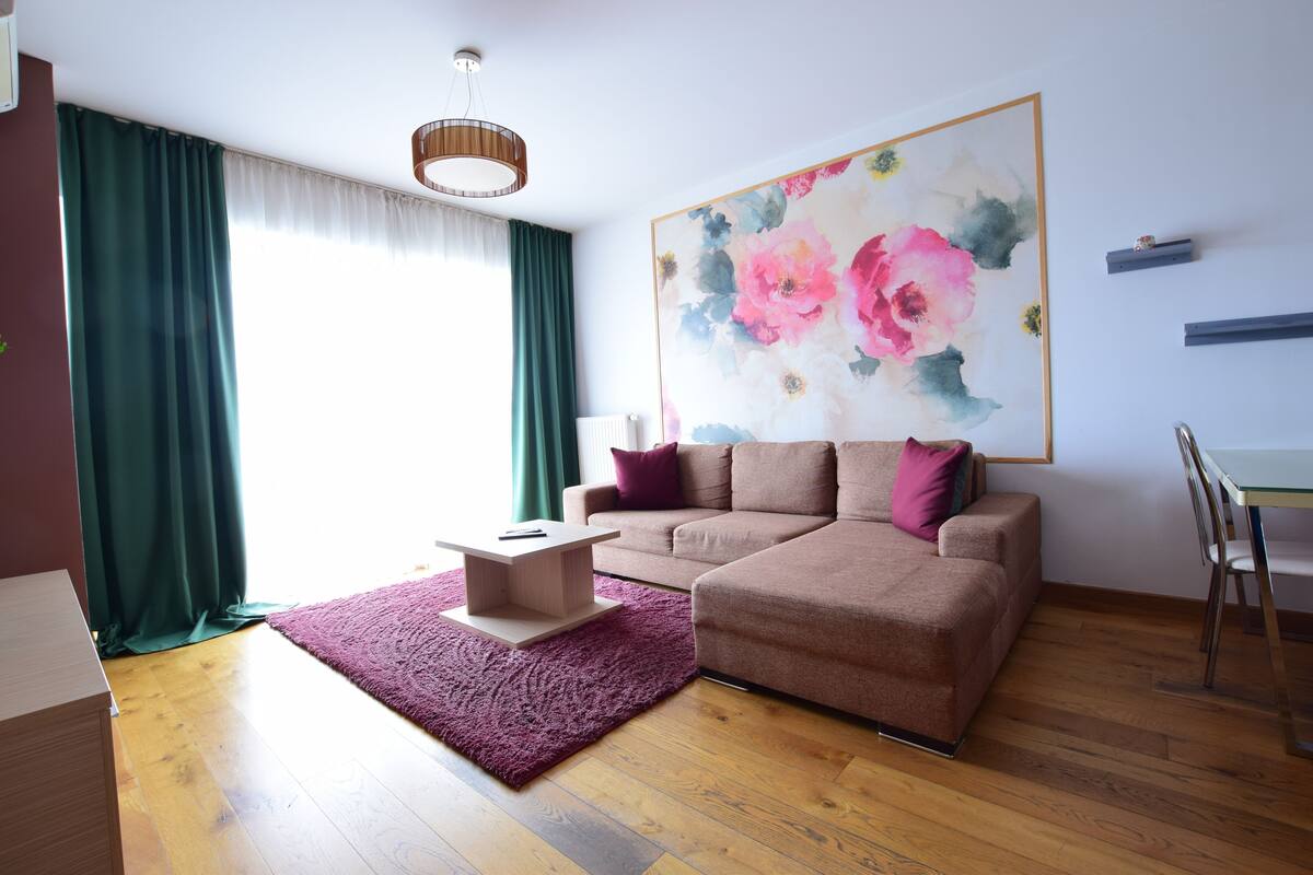 Una sala moderna con un sofá seccional, una mesita de centro y una gran obra de arte floral en la pared.