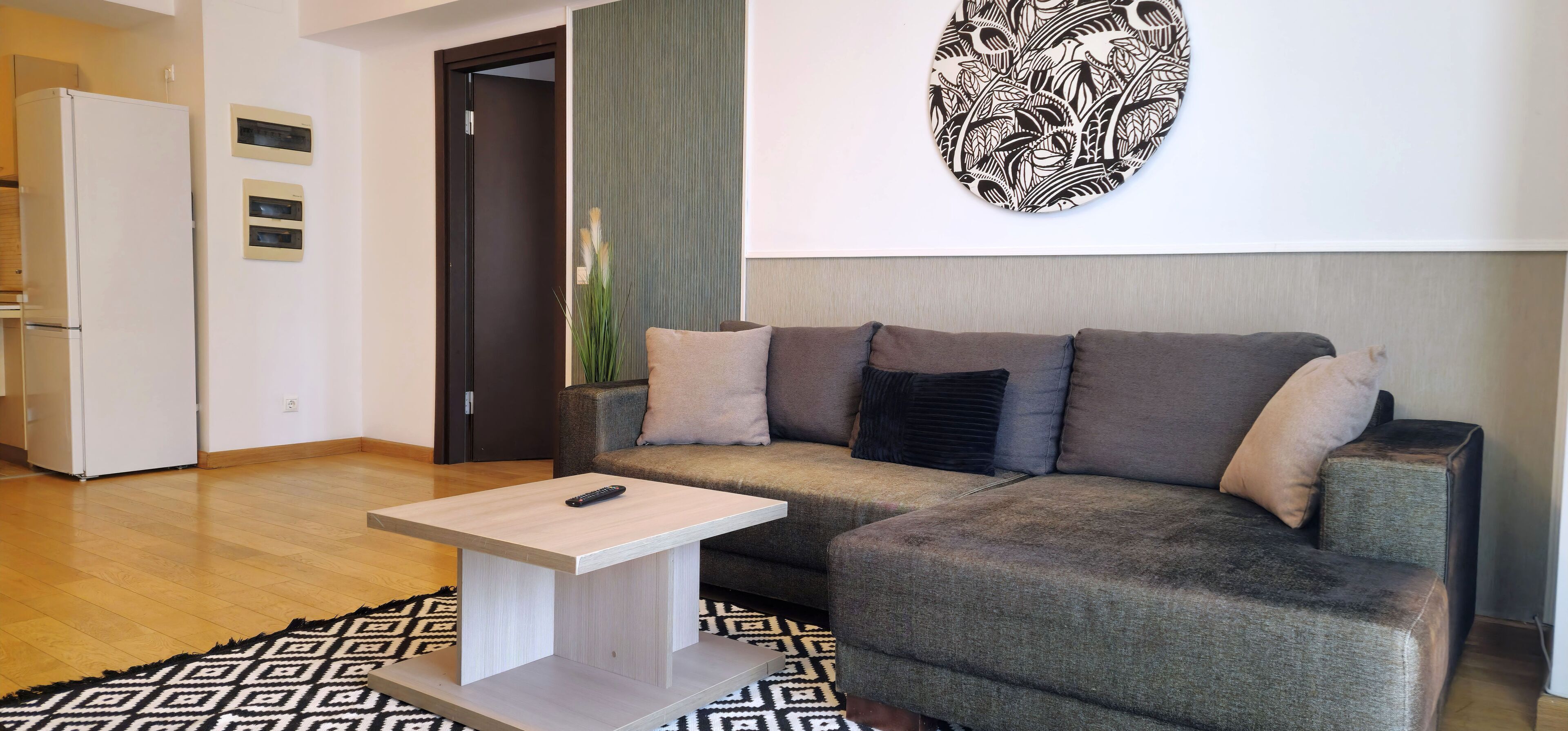Ein modernes Wohnzimmer mit einem grauen Sofa, einem kleinen weißen Couchtisch und einem gemusterten Teppich.