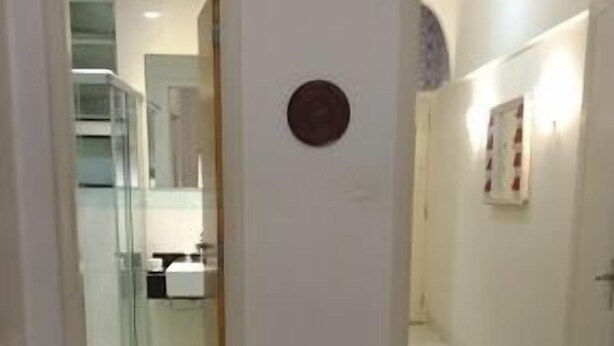 Habitación de hotel con alfombra estampada, un adorno redondo en la pared y una vista parcial de un baño y una cocina a través de una puerta abierta.