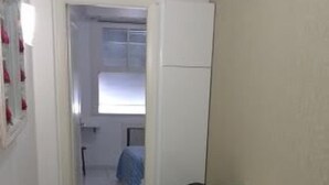 Un pasillo estrecho con suelo de baldosas que conduce a una habitación con una mesa blanca y dos taburetes de madera.