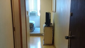 A hallway with a wooden floor, a door on the right, and a television on a stand in the distance. - Kitnet Hilário de Gouveia (Rio de Janeiro)