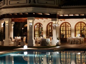 An outdoor dining area with tables and chairs, a pool, and arched windows. - Hotel The Touch Puerto Banús (Marbella)