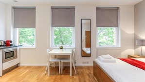Quarto de hotel moderno com piso de madeira, uma escrivaninha branca com duas cadeiras, cama com manta vermelha e um espelho grande.