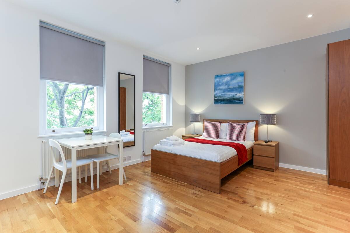 A bedroom with a wooden bed, a desk, and a chair. There are two bedside tables with lamps.