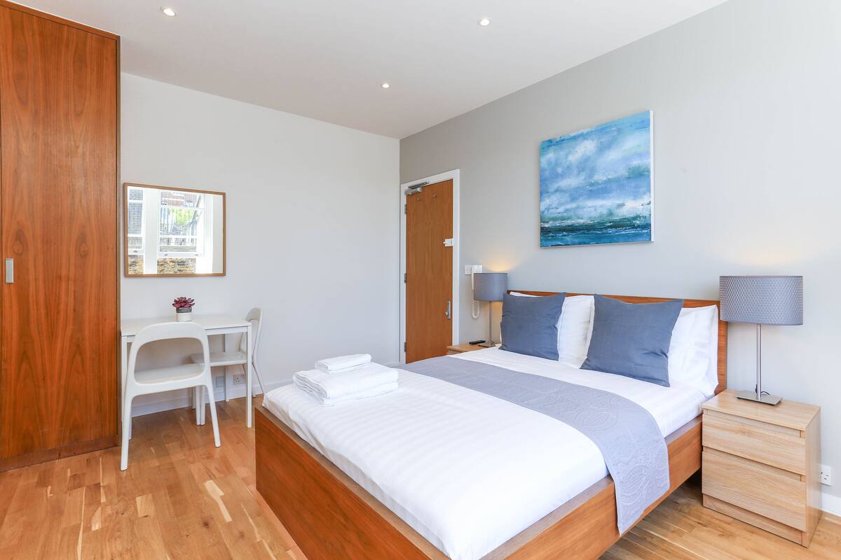 A neatly arranged bedroom with a bed, bedside tables, a desk, and a chair.