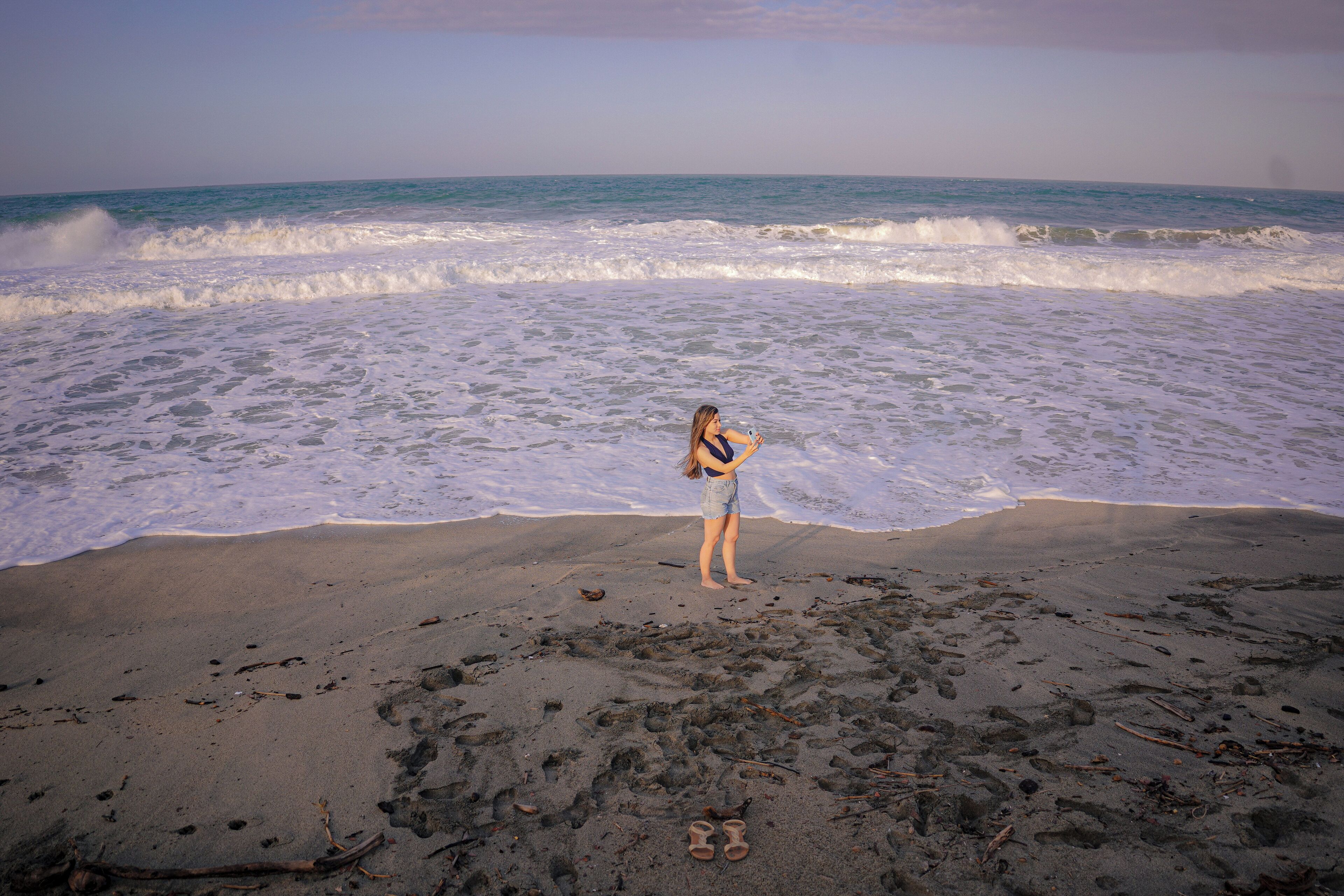 A beach with waves, a person, and scattered debris.