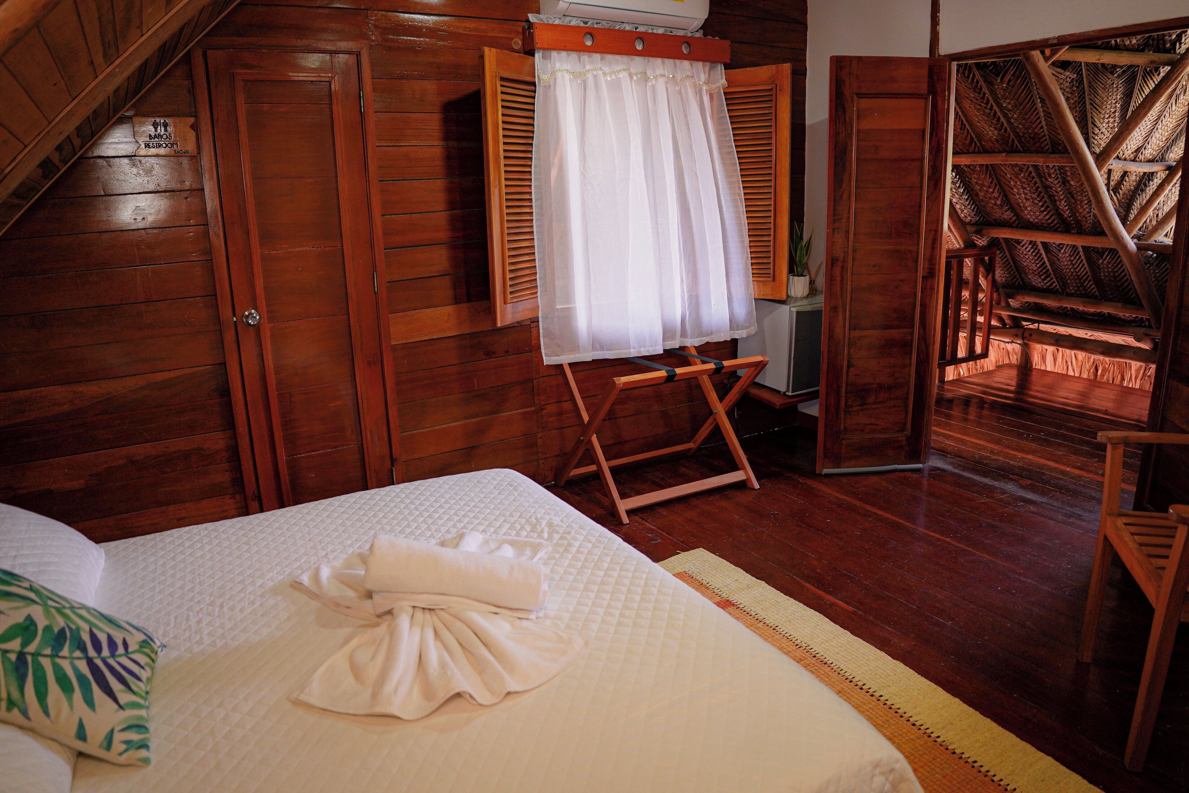 A wooden room with a bed, a small table, and a chair.