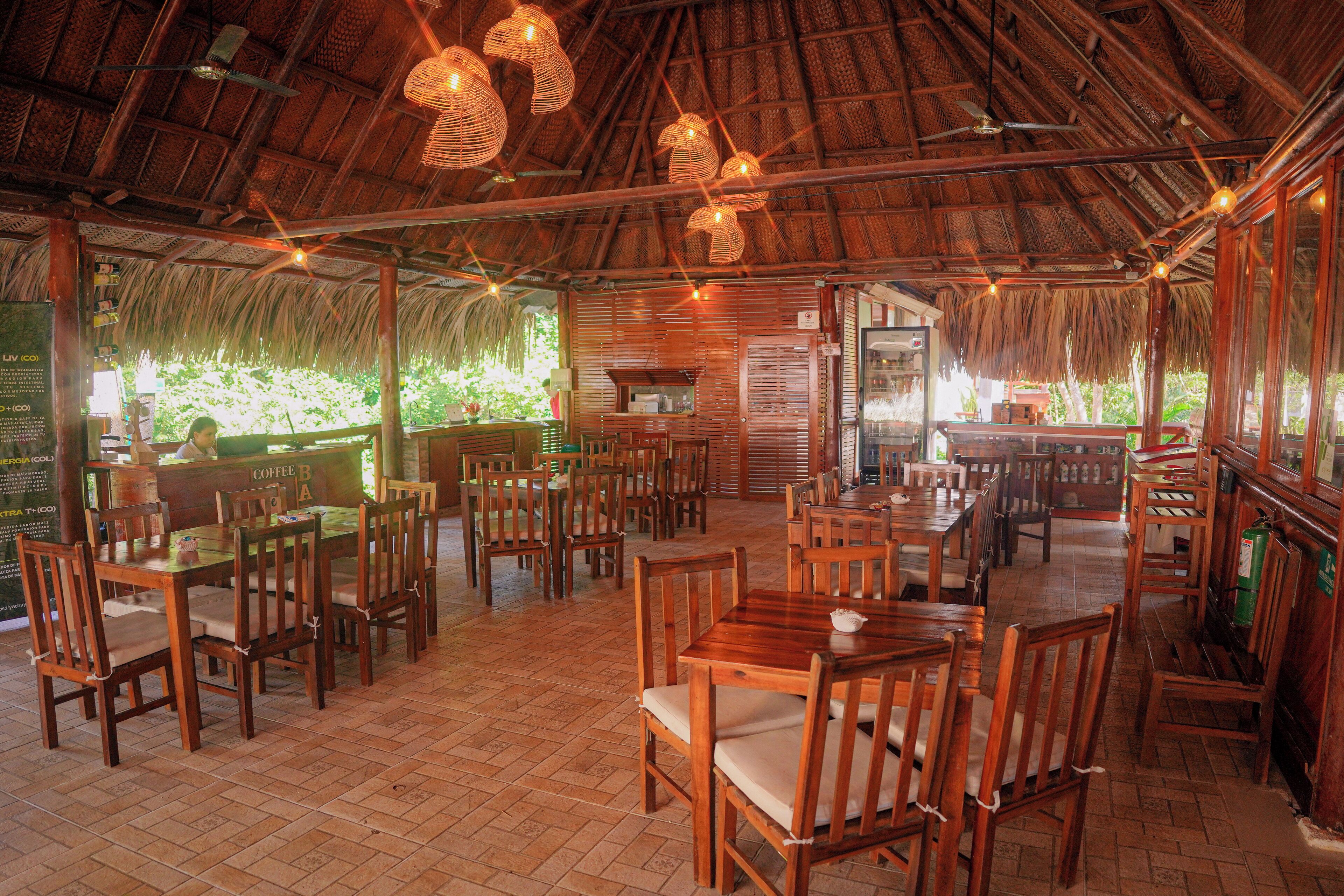 A restaurant with wooden tables and chairs, a thatched roof, and string lights.