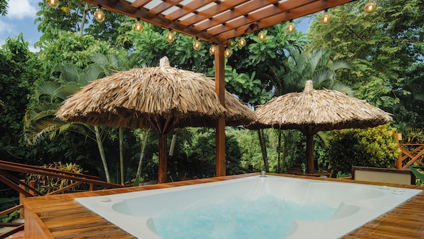 Une terrasse en bois avec un jacuzzi et des parasols en chaume.