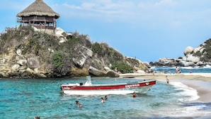 Une plage avec un abri à toit de chaume, une eau turquoise et limpide, et un bateau.