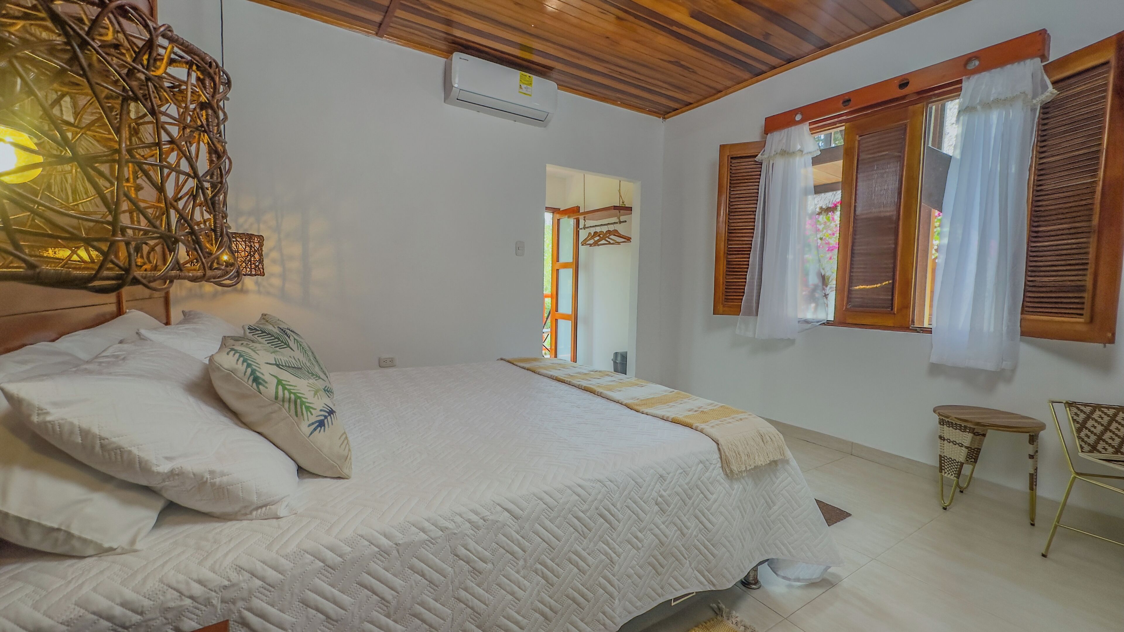 A bedroom with a large bed, a hanging light fixture, and a window with shutters.