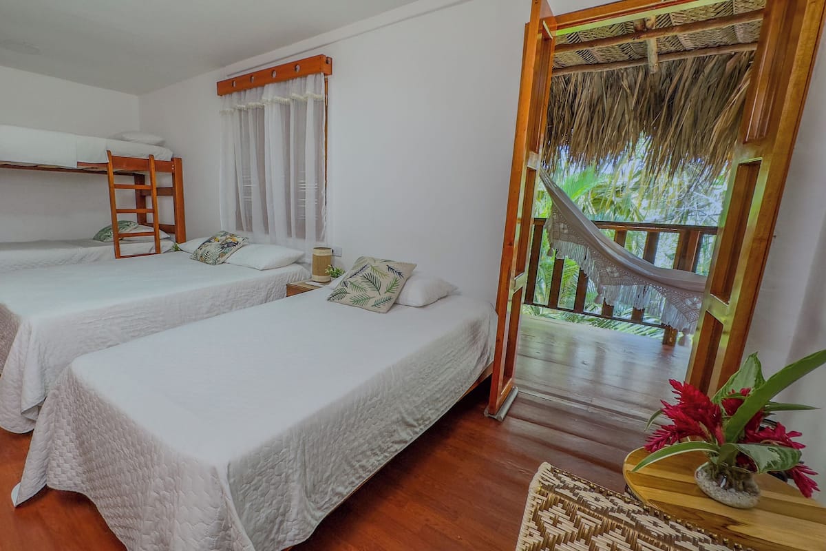A room with two single beds, a wooden ladder, a window with curtains, and a view of greenery outside.