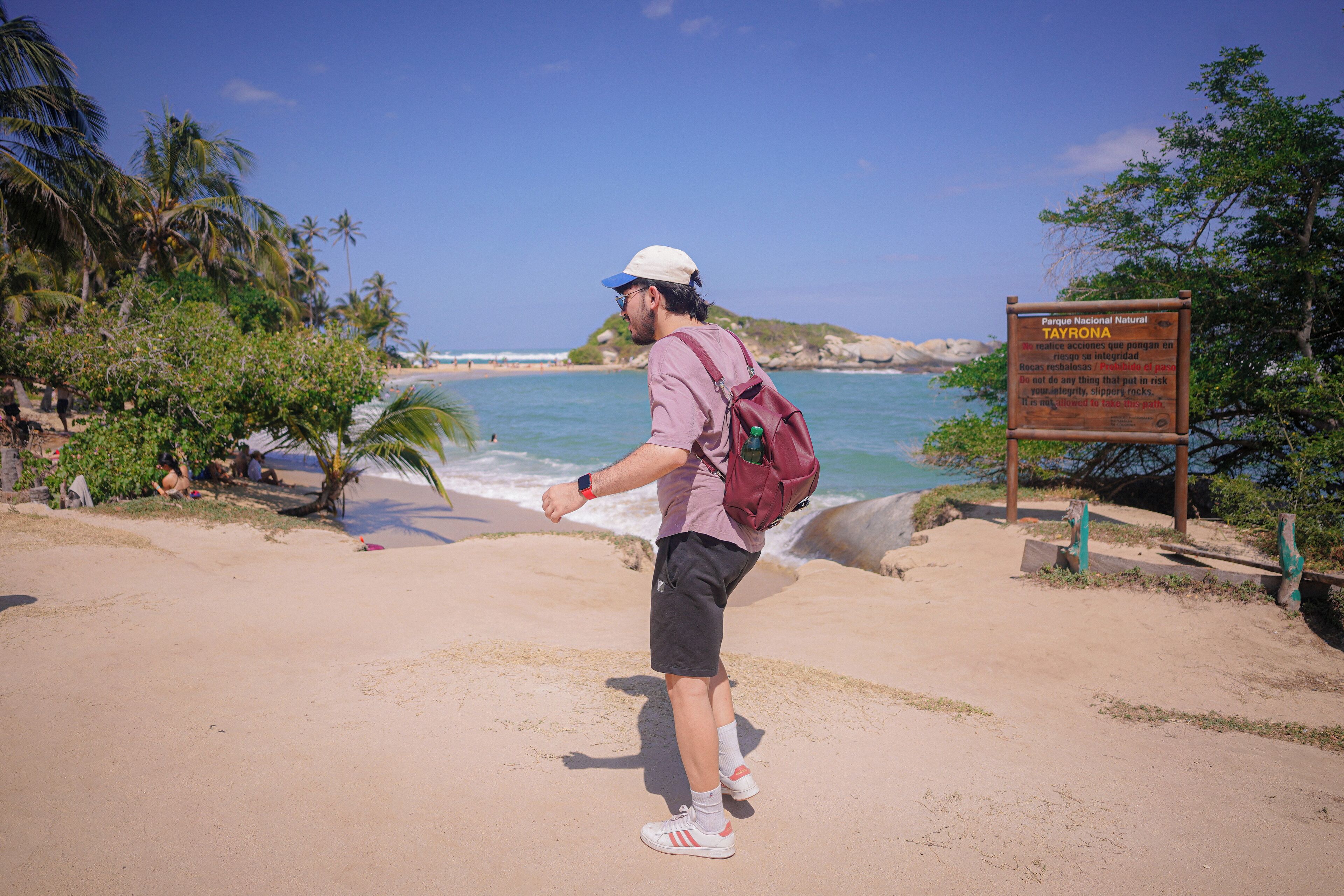 Un hombre está de pie en una playa arenosa, con una mochila, mirando al océano.