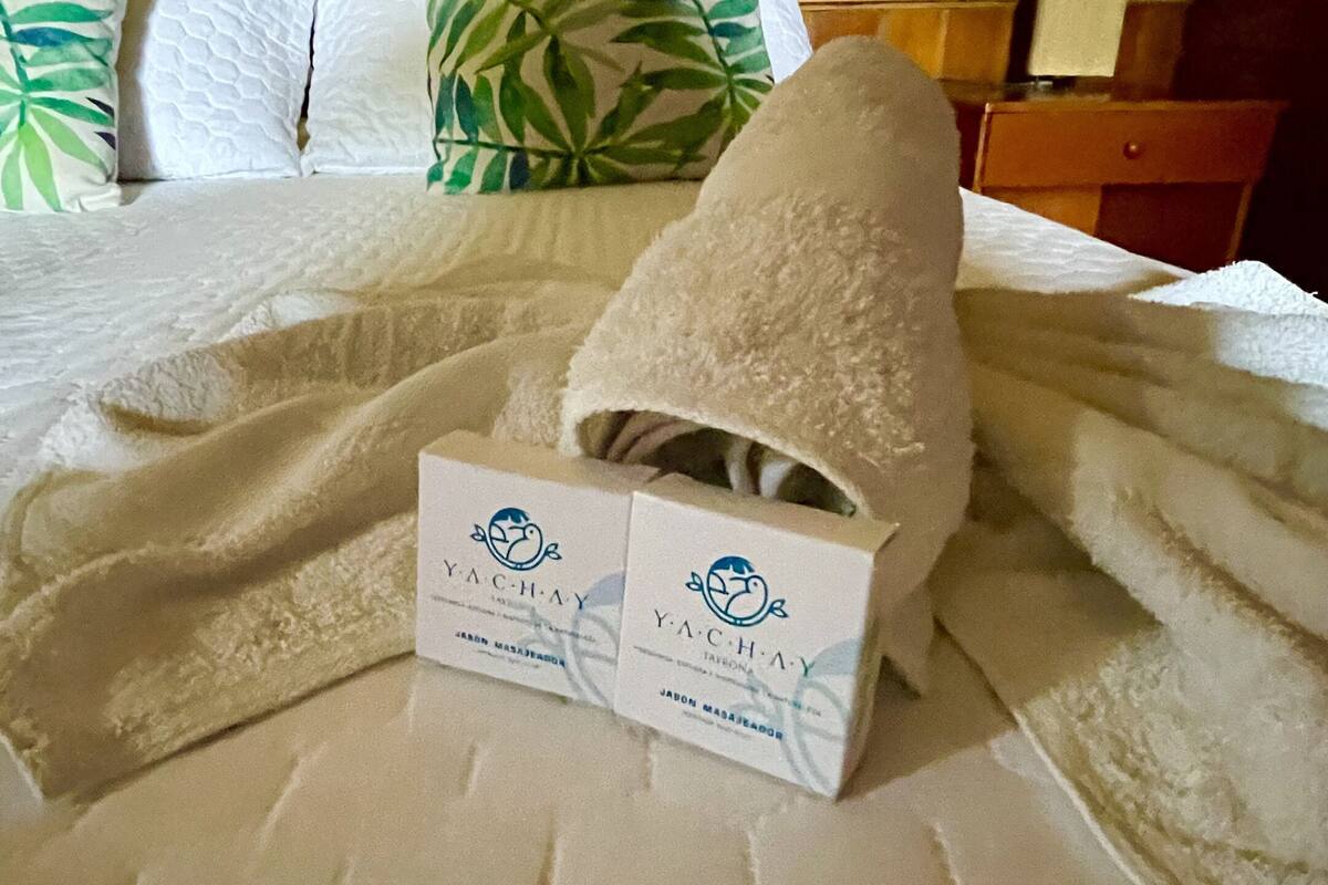 A neatly made bed with a white blanket, a towel, and two boxes labeled 'Yachay'.