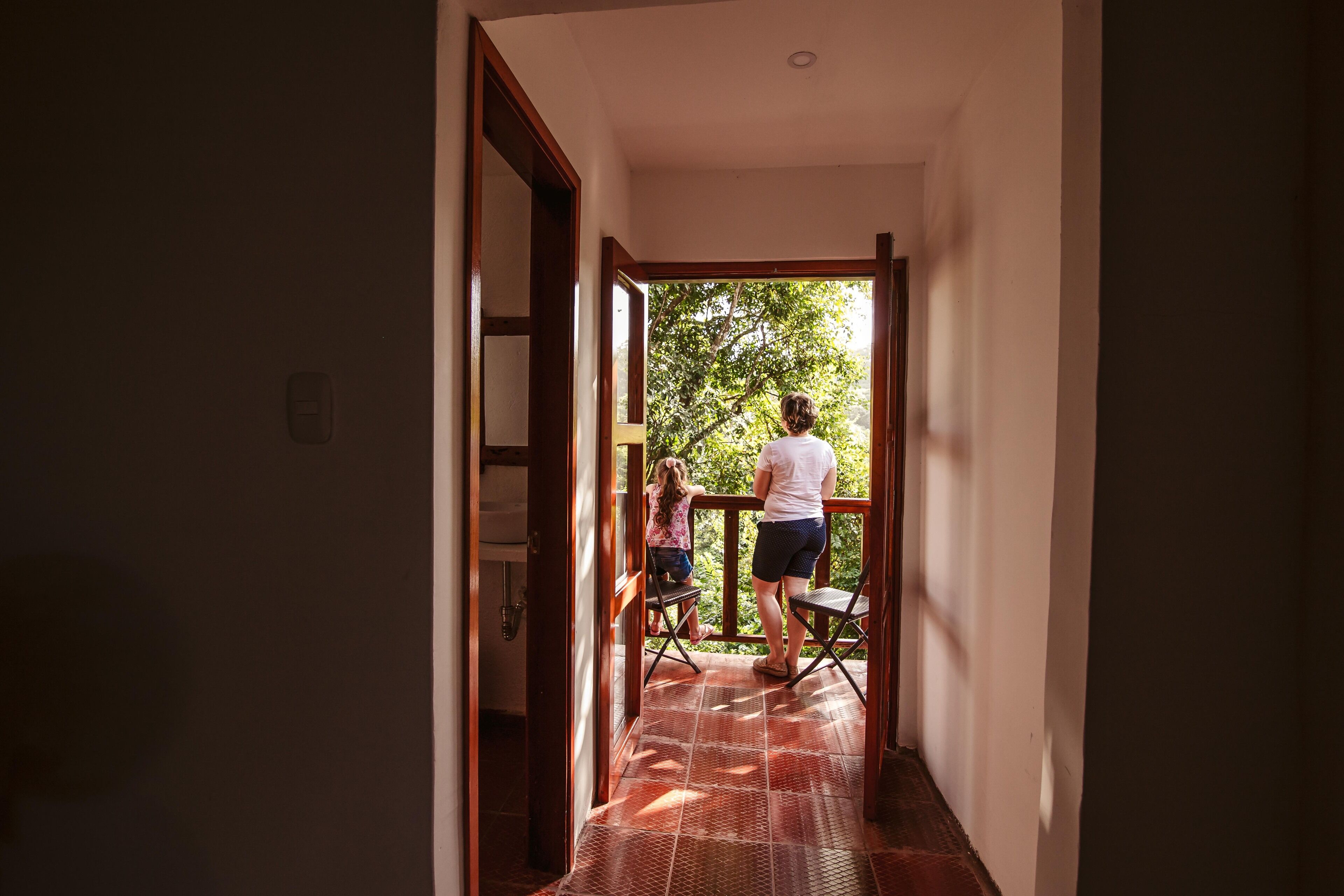 A corridor leading to a balcony with a view of trees.