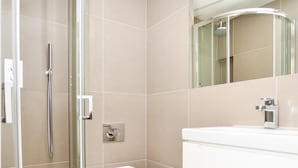 Ein modernes Badezimmer mit einer Glaskabinentrennung zur Dusche, einer weißen Toilette und einem großen Spiegel über einem weißen Waschbecken.
