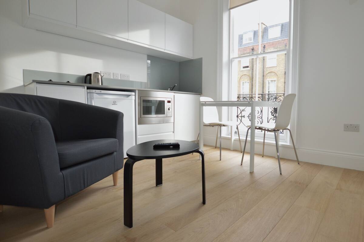 A modern kitchen with white cabinets, a built-in oven, and a dining area with a white table and chairs.