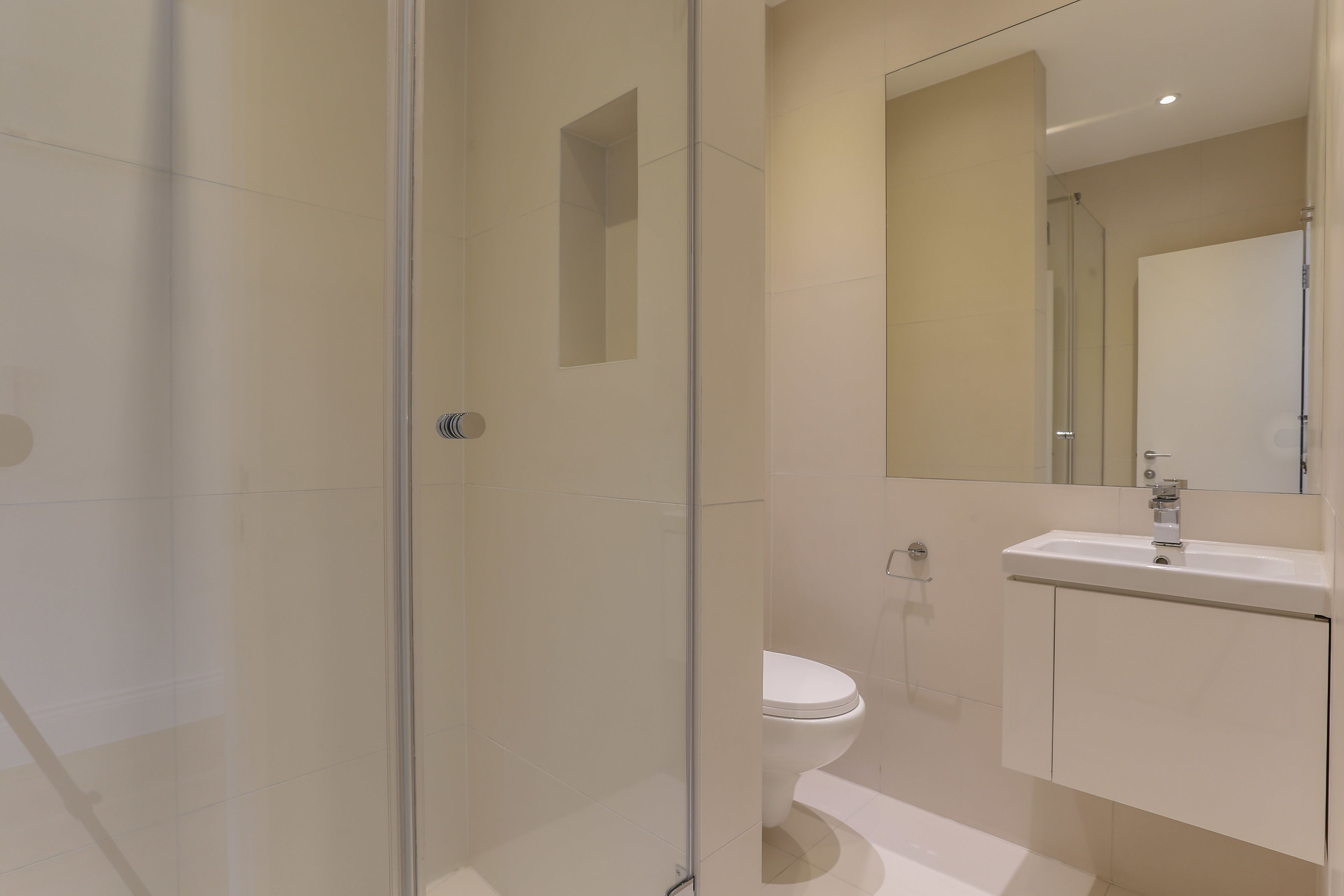 A modern bathroom with a glass shower enclosure, a white toilet, and a sink with a mirror above it.