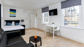Ein modernes Hotelzimmer mit Bett, Schreibtisch, Fernseher und Blick auf die Stadt.