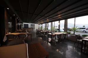 Un'area pranzo interna con tavoli e sedie, ampie finestre e vista sulla strada.