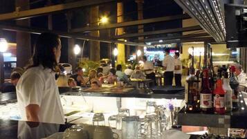 A bar area with tables and chairs, a counter with bottles and glasses, and a view of the street outside.