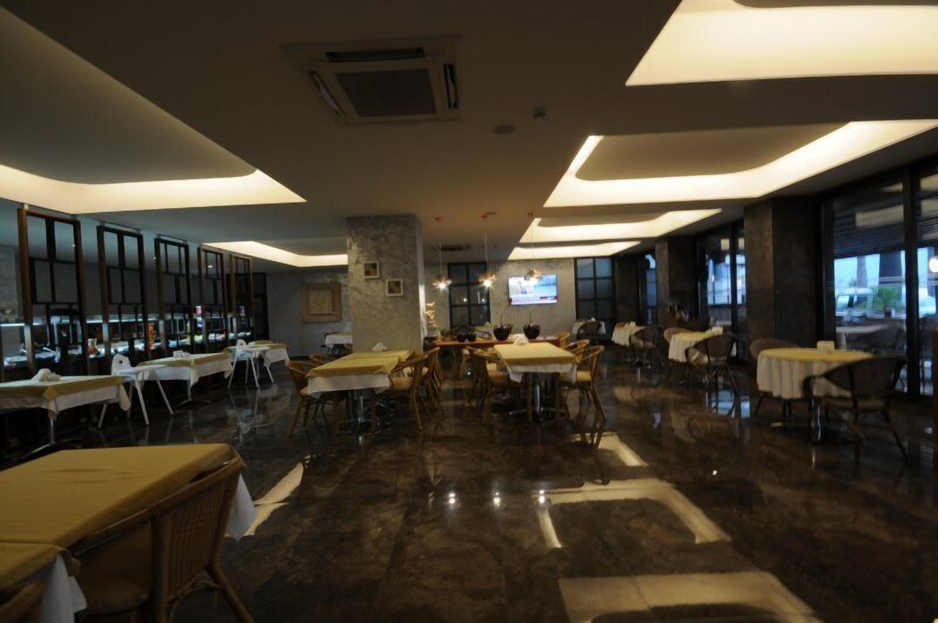 A spacious dining area with multiple tables and chairs, a central pillar, and a television screen on the wall.