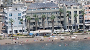 Un hôtel situé sur la côte, avec plusieurs étages, des palmiers et une plage en premier plan.
