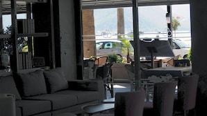 Un intérieur moderne avec un canapé, des fauteuils et une table. Une grande fenêtre offre une vue sur les voitures garées et la verdure à l’extérieur.